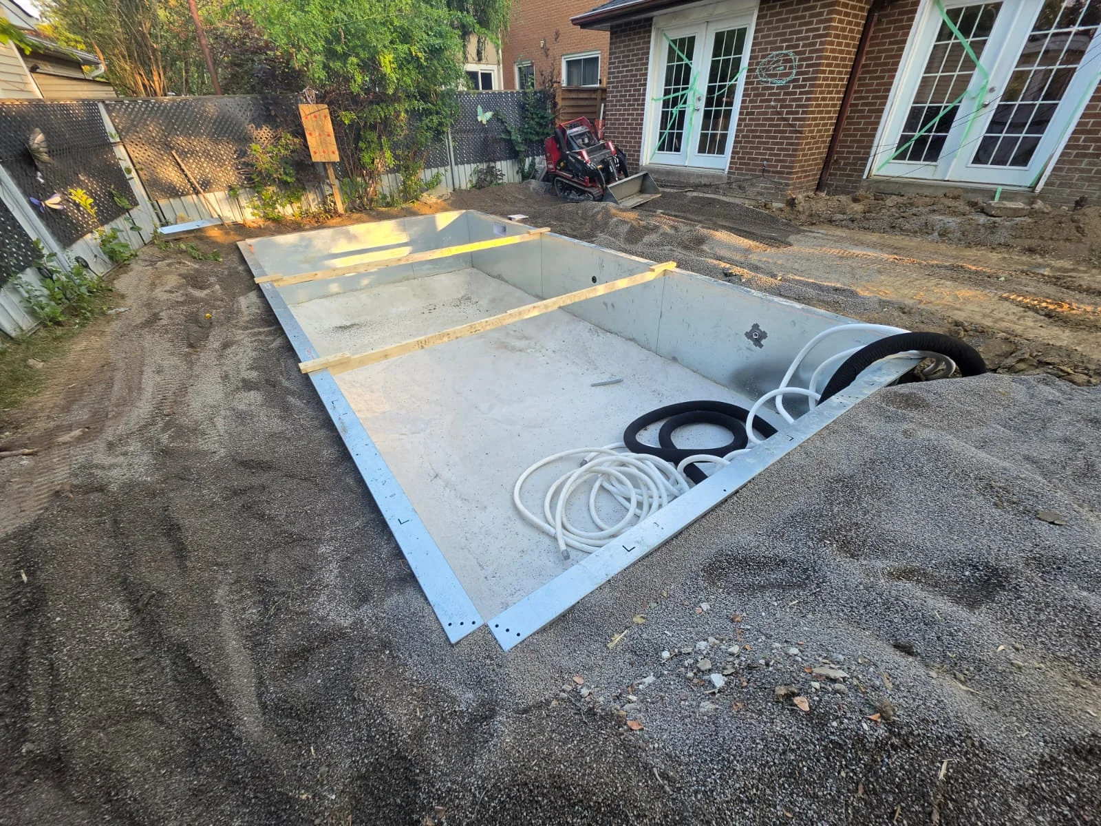 Rectangular pool shell during construction beside a brick house