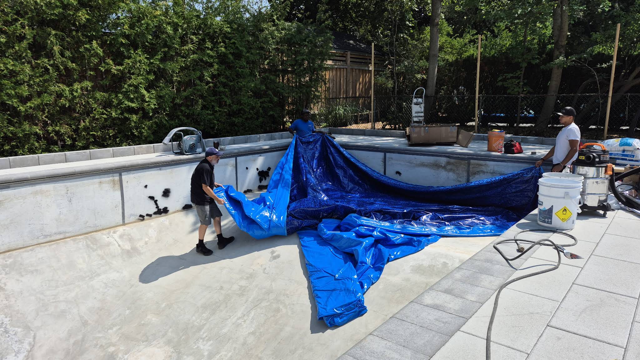 Three OPS installers positioning a new blue patterned vinyl liner in the pool